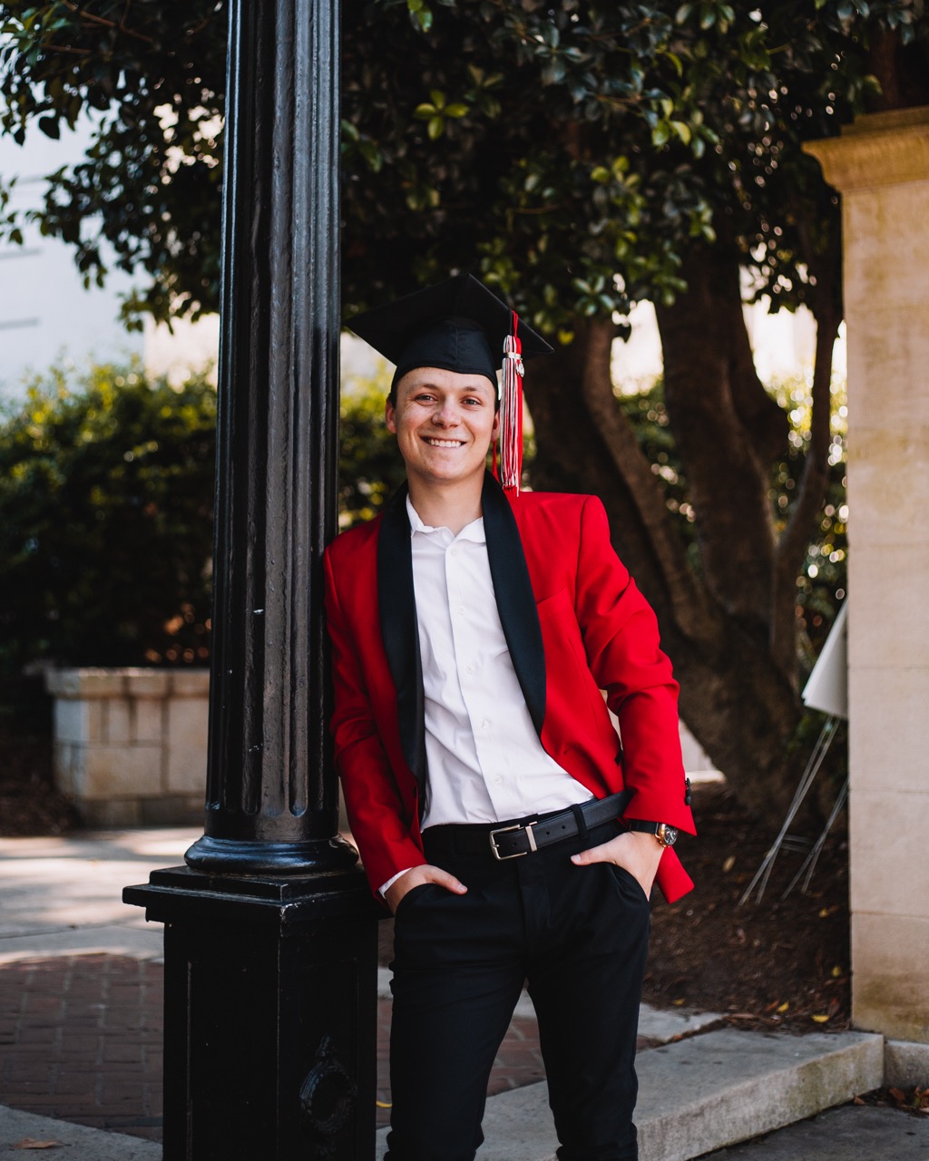 Bailey Pelletier with a graduation cap and red blazer leaning against the UGA arch